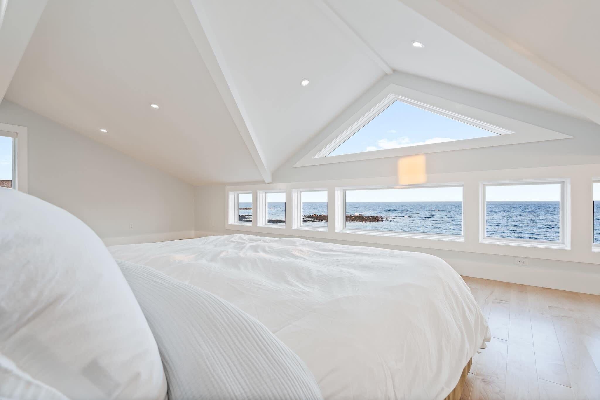 Un dormitorio con una cama grande, tragaluz y vista al océano.