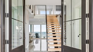 A modern interior with a glass door leading to a spacious area with a wooden staircase and a view of the sea. - Brand New Home Ocean Views Wolf Appliances (Wells)