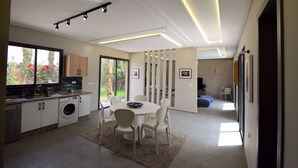 A modern kitchen with a built-in washing machine, a dining area with a round table and chairs, and a living area with a sofa and a TV.