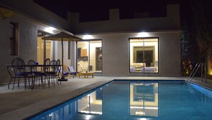 An indoor swimming pool with a sunken seating area and a table with chairs.