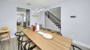 Un espace repas moderne avec une table en bois, des chaises et une chaise haute pour bébé. On aperçoit un escalier à l’arrière-plan.