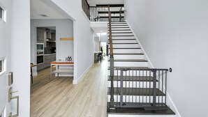 Un intérieur moderne avec un escalier menant à un niveau supérieur, un coin cuisine et un espace repas comprenant une table et des chaises en bois.