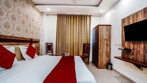 A hotel room with a large bed, a TV mounted on the wall, a wardrobe, and a ceiling fan. - Hotel Almond (Zirakpur)