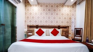 A hotel room with a large bed, a wooden headboard, a patterned wallpaper, and a glass door. - Hotel Almond (Zirakpur)