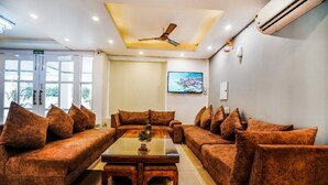 A hotel lobby with a sofa set, a coffee table, a ceiling fan, a TV, and a fire exit sign. - Hotel Almond (Zirakpur)