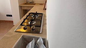 A compact kitchen with a gas stove, a sink, and a shelf above the counter. - Casaggiù traditional house just steps from the towncenter & seaside destinations (San Vito dei Normanni)