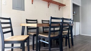 Een eetruimte met een houten tafel en zes stoelen, een wandplank en een deur die naar een andere kamer leidt.