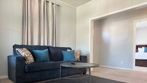 Een moderne woonkamer met een donkerblauwe bank, kussens met een patroon, een klein rond tafeltje en een neutraal vloerkleed.