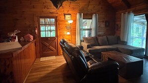 Interior acogedor de una cabaña con un sofá de cuero, un comedor y techo de madera.