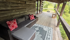 Un área de estar al aire libre techada con un banco de madera y cojines, un tapete estampado y vistas al verdor.