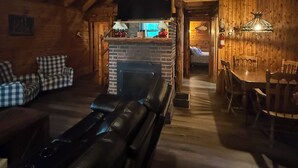Acogedor interior de cabaña de troncos con chimenea, sofá de cuero, mesa de comedor y paredes de madera.