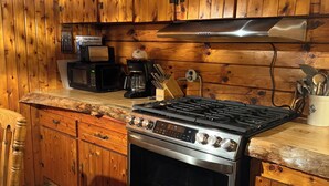 Una cocina con gabinetes de madera, estufa de acero inoxidable, cafetera y un bloque de cuchillos.