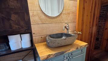 A bathroom with a stone sink, wooden wall paneling, a mirror, and a toilet.