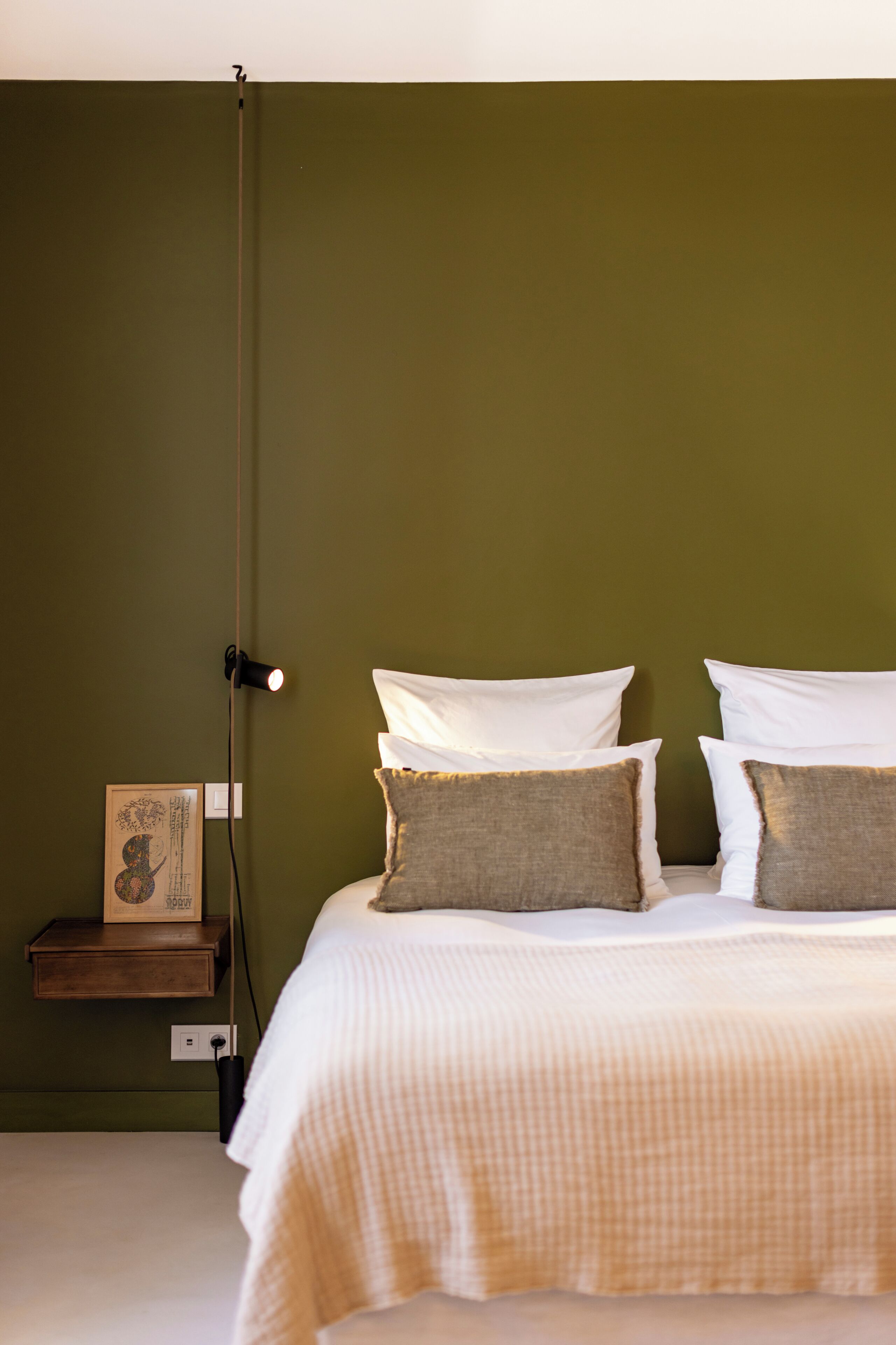 A bed with white bedding and two pillows, a bedside table with a lamp, and a framed picture on the wall.