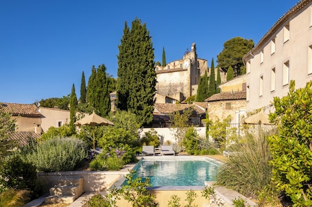A pool surrounded by greenery and traditional architecture.. La Maison des Jardins
