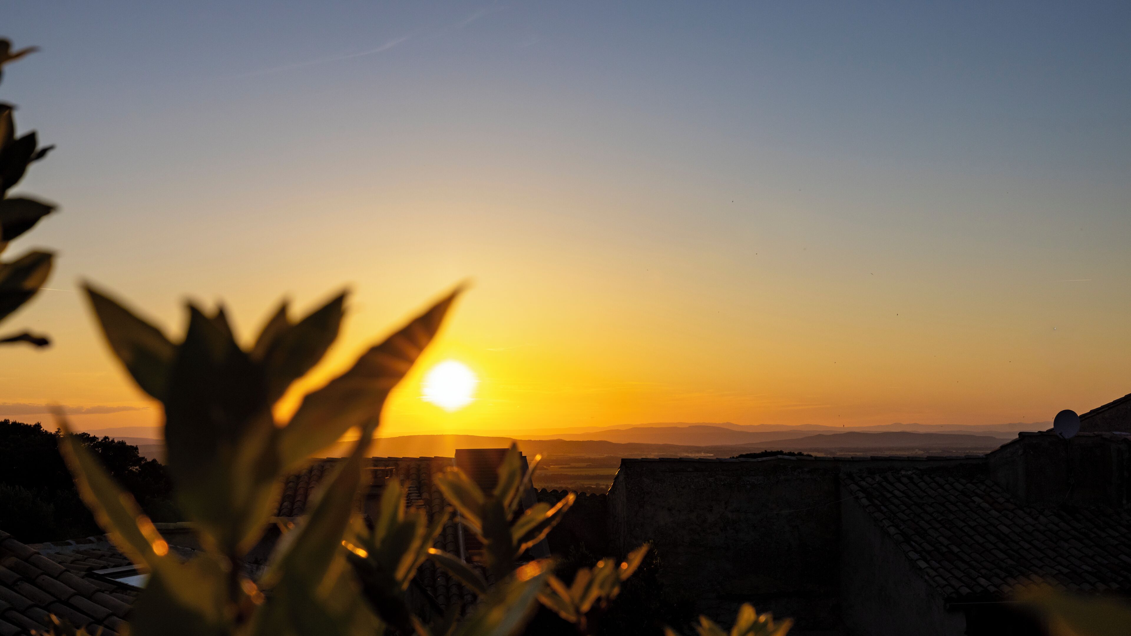 Un coucher de soleil sur un paysage montagneux, avec en arrière-plan des bâtiments traditionnels.