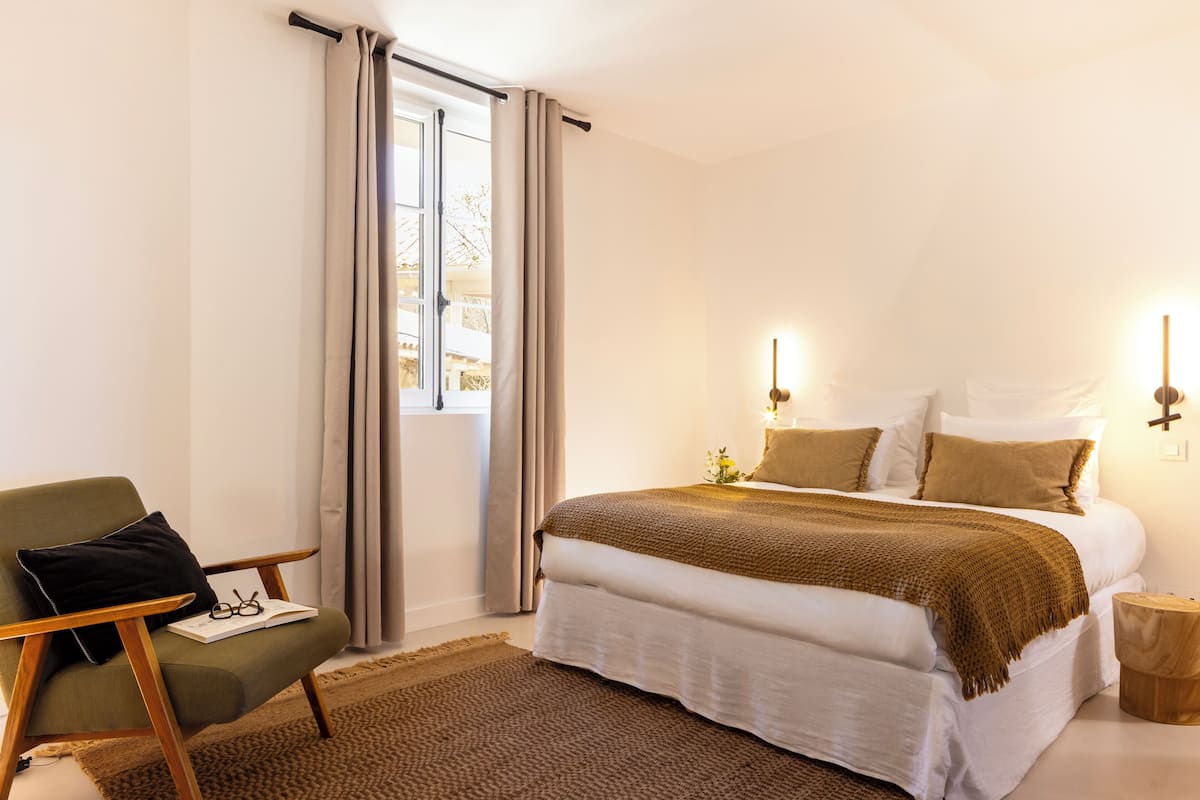 Un dormitorio con una cama, una silla, una ventana con cortinas y una mesita de noche.