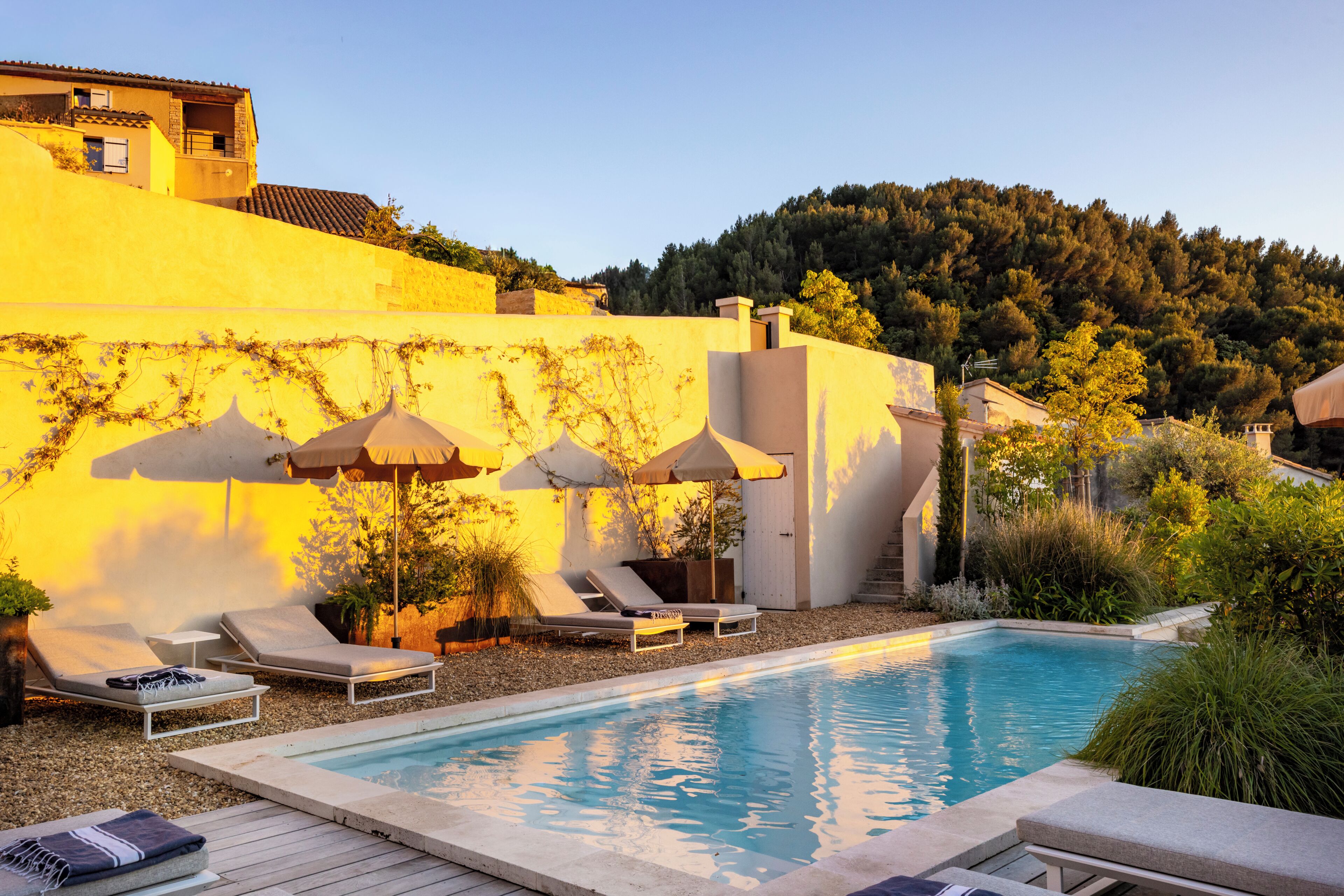 Área de piscina com espreguiçadeiras, guarda-sóis e vista para uma encosta.