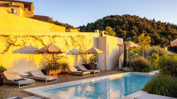 Área de piscina com espreguiçadeiras, guarda-sóis e vista para uma encosta.