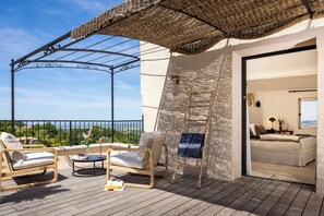 A balcony with a wooden floor, a wicker umbrella, two lounge chairs, a small round table, and a view of the sea. - La Maison des Jardins (Gigondas)