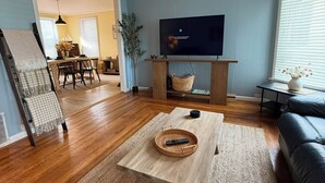 A living room with a TV, a coffee table, a sofa, and a dining area in the background. - Lake Breeze Cottage.   
One block from the lake, walking distance to downtown! (Sheboygan)