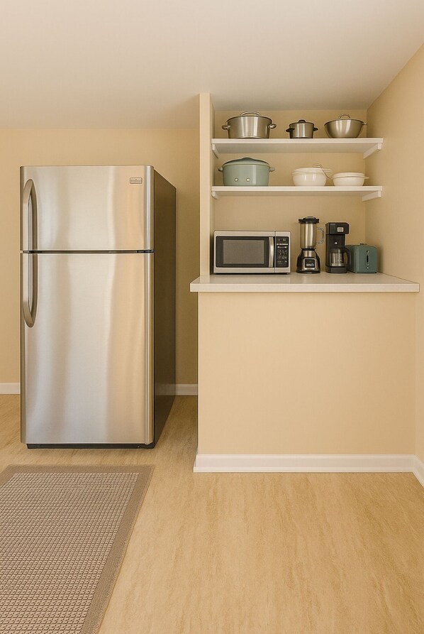 Cocina compacta con refrigerador de acero inoxidable, microondas, cafetera y licuadora sobre la encimera.