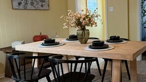 A dining area with a wooden table, black chairs, a vase with flowers, and a hanging light fixture. - Lake Breeze Cottage.   
One block from the lake, walking distance to downtown! (Sheboygan)