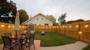 A backyard with a wooden fence, a dining table with chairs, and a covered patio area. - Lake Breeze Cottage.   
One block from the lake, walking distance to downtown! (Sheboygan)