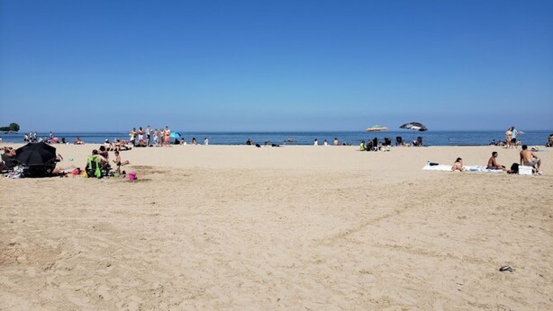 A beach with people sunbathing and swimming, umbrellas, and beach chairs. - Lake Breeze Cottage.   
One block from the lake, walking distance to downtown! (Sheboygan)