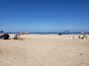 Una playa con gente tomando el sol y nadando, sombrillas y sillas.