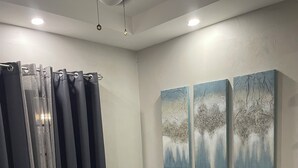 A room with a blue sofa, two paintings on the wall, a ceiling fan, and a curtain. - Fantastic modern apartment in Chaguanas (Chaguanas)