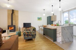 Et moderne køkken med indbygget komfur, et spiseområde med bord og stole, og et stort vindue der giver naturligt lys.