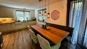 A modern kitchen with a wooden dining table, light-colored cabinets, and a decorative wall piece. - Detached country house in Drenthe with large garden, terrace & beautiful views (Schoonloo)