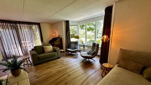 A living room with a sofa, armchairs, a piano, and a large window with curtains. - Detached country house in Drenthe with large garden, terrace & beautiful views (Schoonloo)
