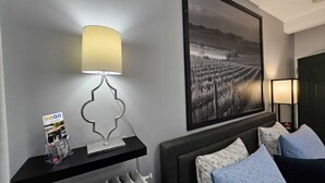 Habitación de hotel con cama, mesita de noche con lámpara, fotografía en blanco y negro enmarcada en la pared y una revista sobre la mesita de noche.