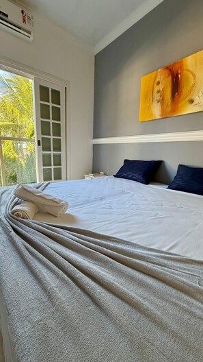 Un letto rifatto con cura, un asciugamano piegato, un comodino, un quadro appeso e una finestra con vista sul verde.