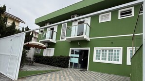A two-story building with a green facade and white trim. There are multiple windows with white shutters, and a covered patio area with a table and chairs.