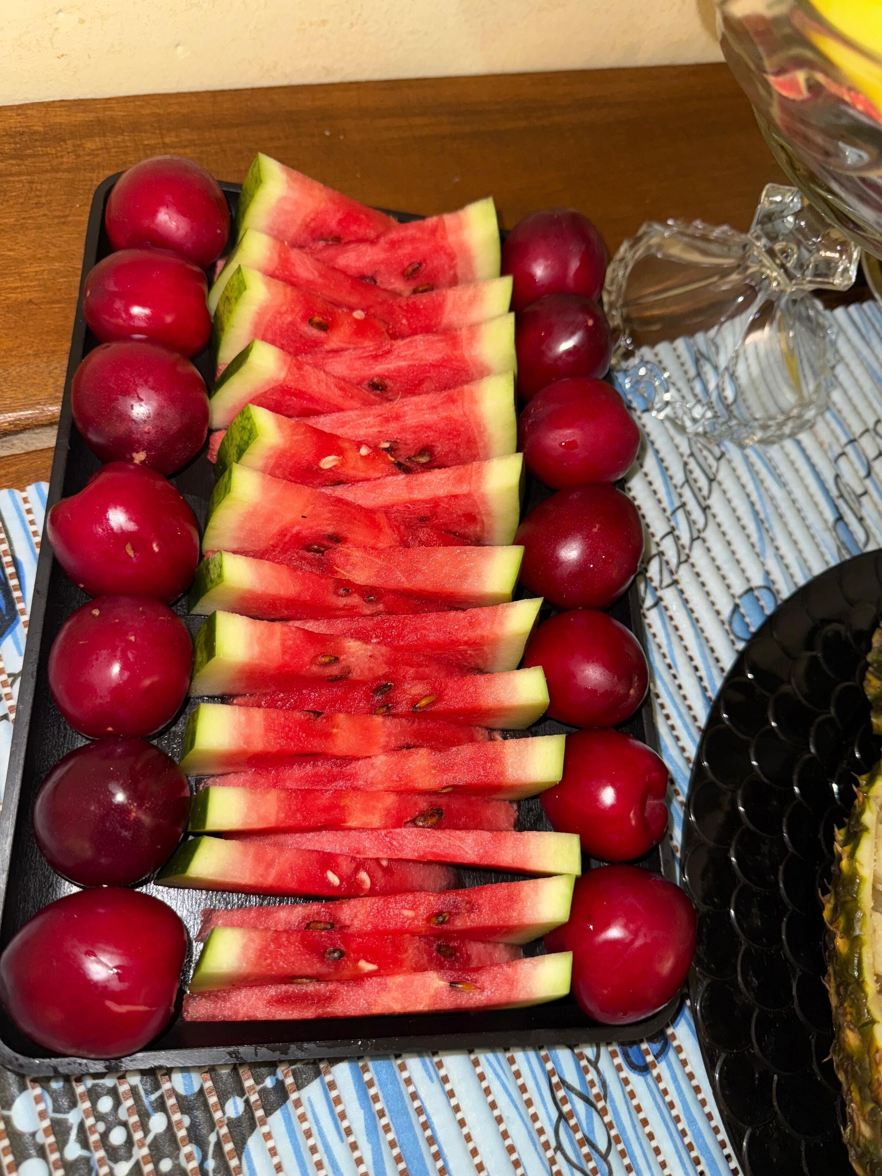 Uma bandeja com melancia fatiada e uvas vermelhas sobre uma toalha estampada.