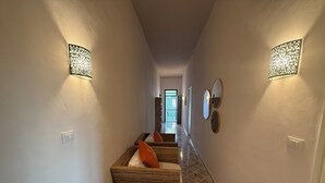 A hallway with a woven bench, wall sconces, and a tiled floor. - Villa Sole (Petrosino)