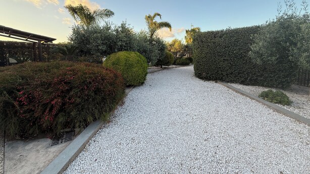 A gravel pathway flanked by neatly trimmed hedges and shrubs, leading to a covered area with a pergola. - Villa Sole (Petrosino)