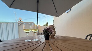 A wooden table with two wine glasses under an umbrella, a potted plant, and a view of the sky and buildings. - Villa Sole (Petrosino)