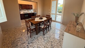 A kitchen with wooden cabinets, a dining table with chairs, and a terrazzo floor. - Villa Sole (Petrosino)