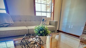 A modern living room with a glass coffee table, a geometric metal sculpture, a potted plant, and a sofa with a cushion. - 4 Bedroom Family Friendly Home in Great Madison Location (Madison)