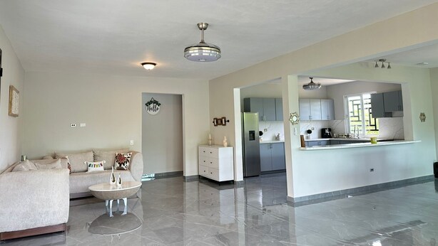 Amplia sala de estar con sofá, mesa de centro y una zona de cocina con armarios y refrigerador.