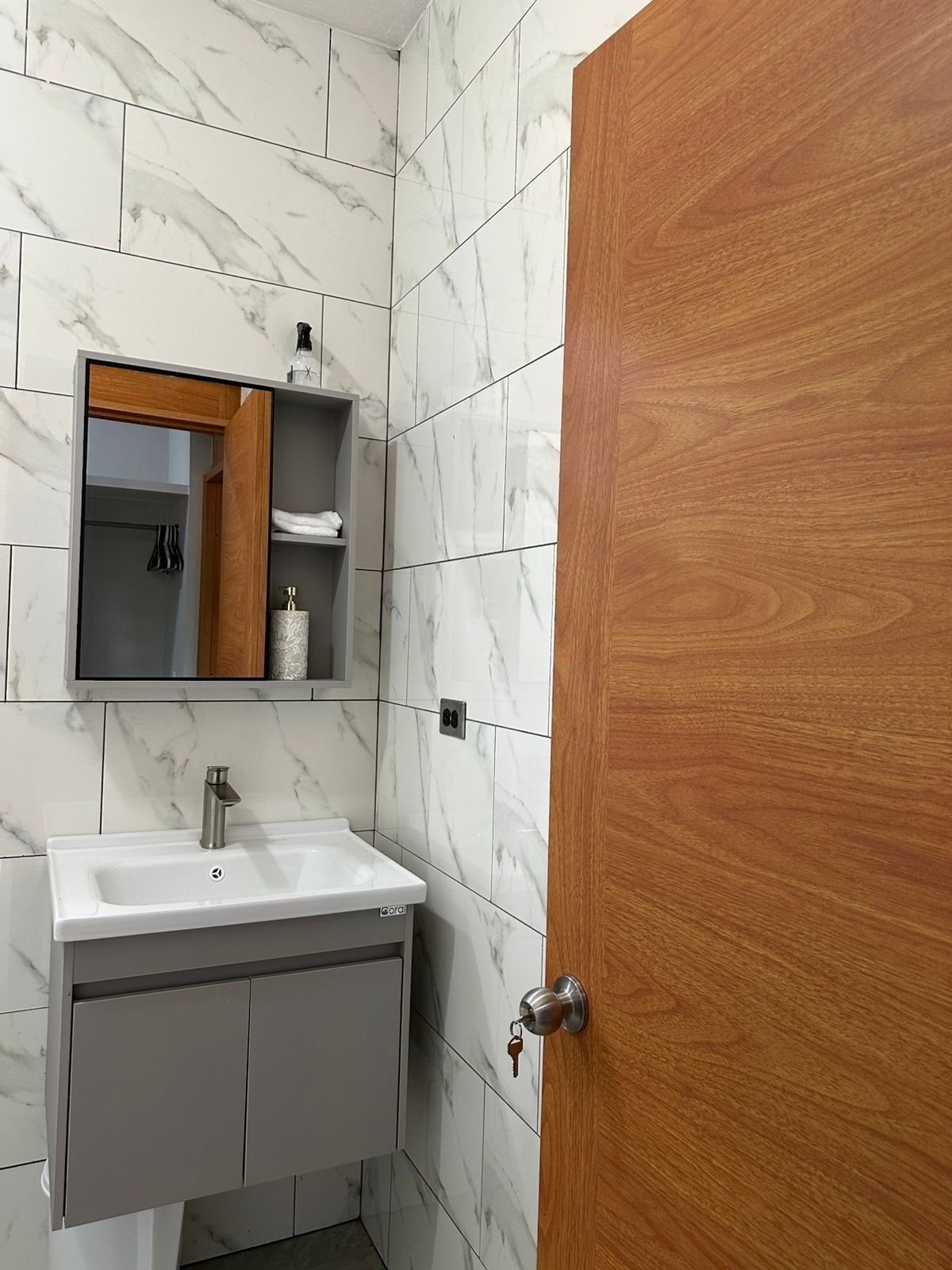 A bathroom with a white marble tile wall, a white sink with a modern faucet, a wooden door, and a mirror above the sink.