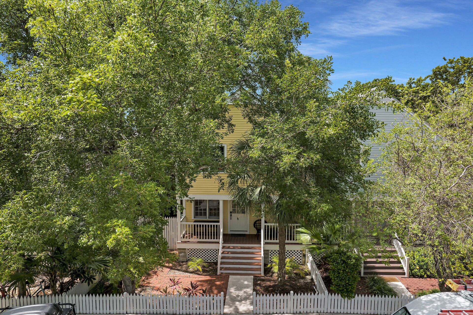 A yellow house with a porch, surrounded by trees and a white picket fence.