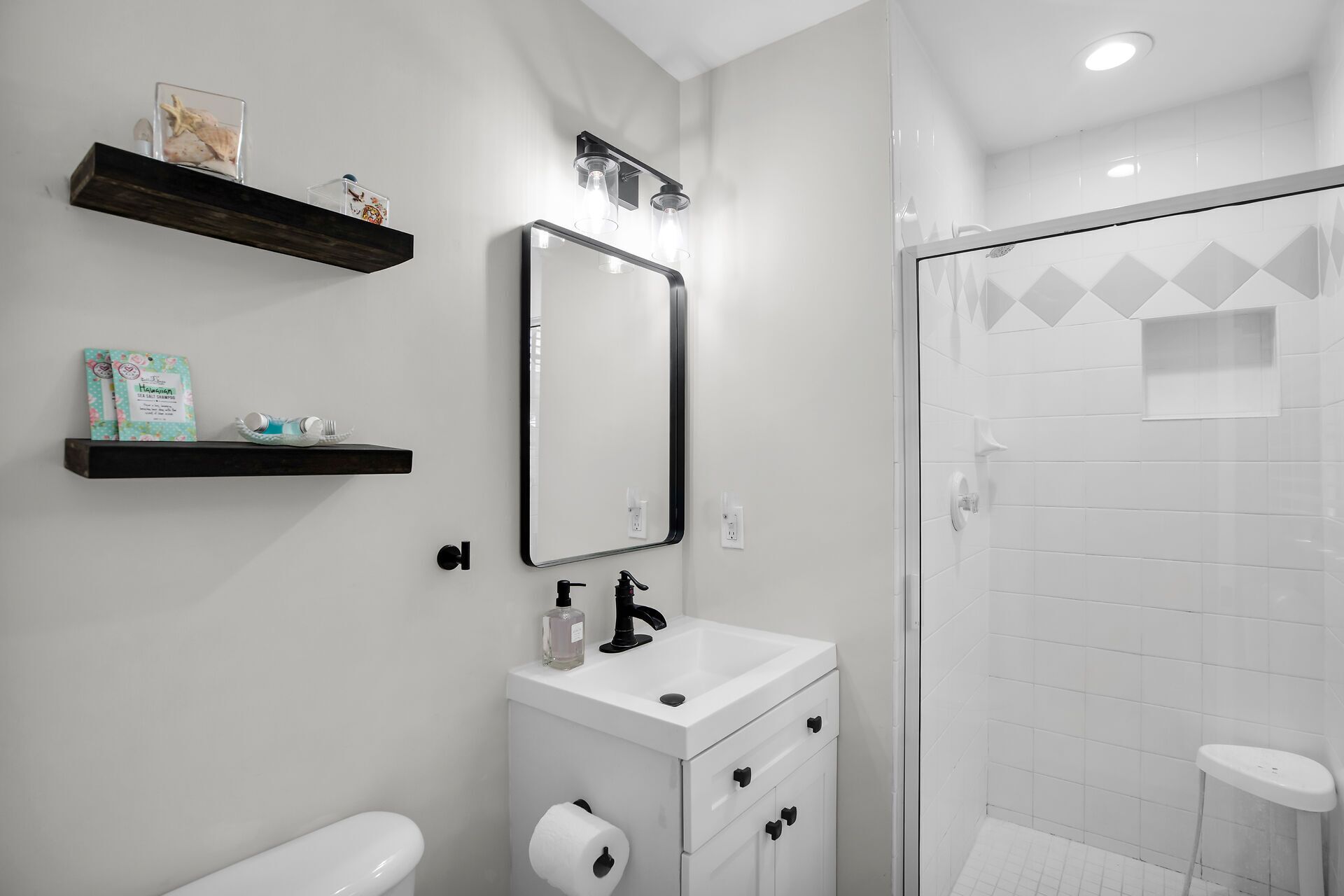 A modern bathroom with a toilet, sink, and shower. There are two shelves with decorative items and a mirror above the sink.