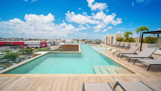 A rooftop pool with clear blue water, lounge chairs, and a view of the cityscape. - 1 Bedroom Condo Pool & Gym - Veranto 210 (Playa del Carmen)