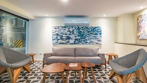 A modern lounge area with a geometric patterned floor, a grey sofa, and two woven chairs. - 1 Bedroom Condo Pool & Gym - Veranto 210 (Playa del Carmen)