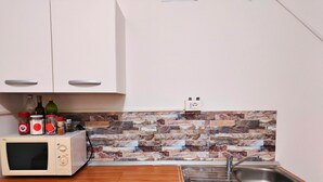 Et køkken med hvide skabe, en mikroovn, en vask og en backsplash i sten.